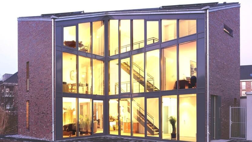 Moderne, mehrst&ouml;ckige Wohnung mit gro&szlig;fl&auml;chigen Fenstern und Treppe, beleuchtet bei D&auml;mmerung.