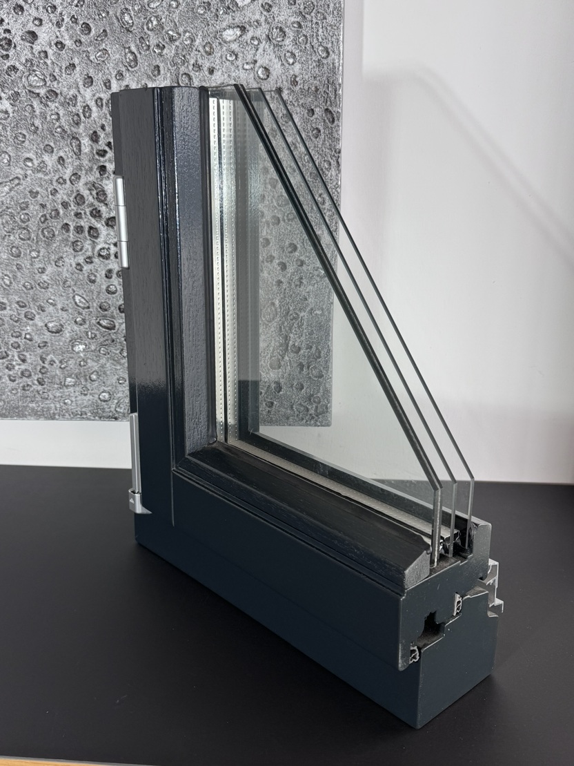 Detailaufnahme eines Fensterprofils mit drei Scheiben, montiert auf einem schwarzen Tisch, im Hintergrund eine strukturierte Wand.