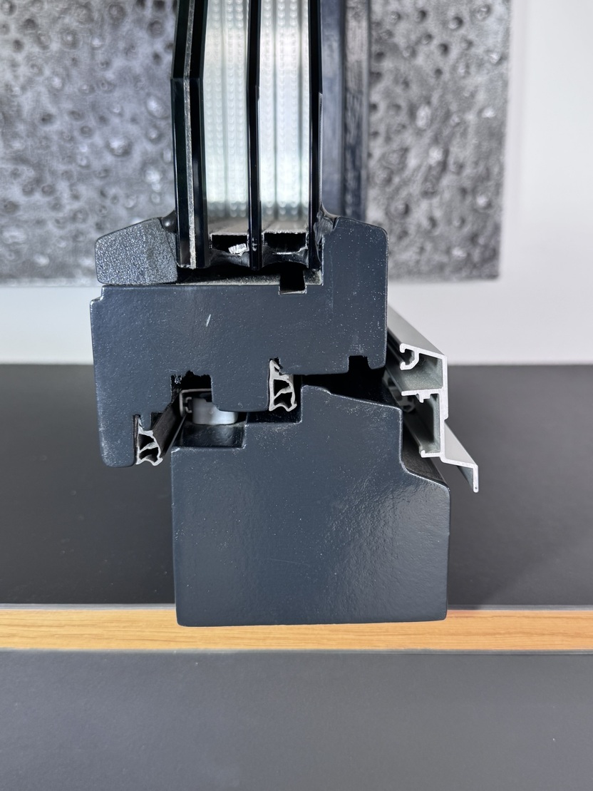 Detailaufnahme eines Schnitts durch einen schwarzen Fensterrahmen mit Glaselementen und Aluminiumprofilen.