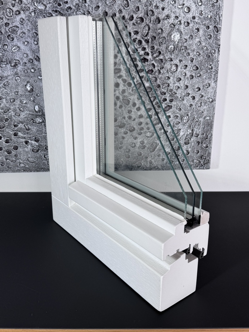 Detailaufnahme eines Fensters mit drei Glasschichten und wei&szlig;em Rahmenelement vor einer grauen Wand.