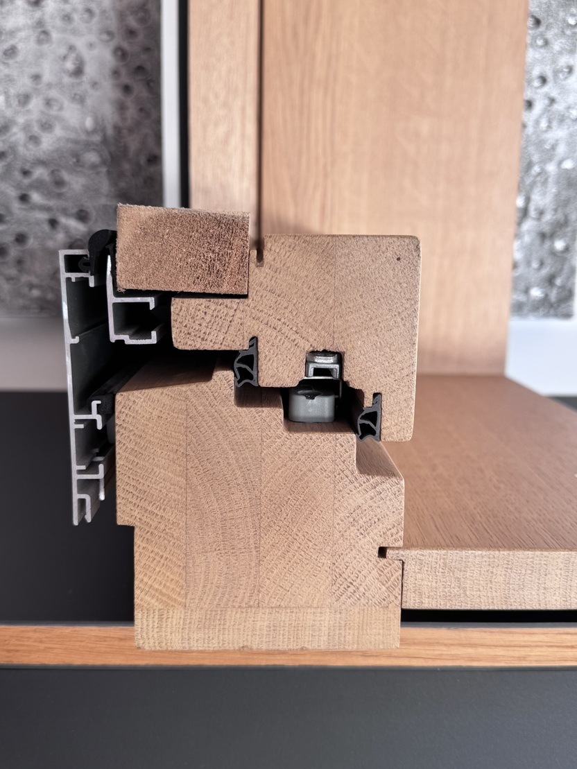 Schnittansicht eines Holzprofils mit Kunststoffelement und Metalldetails auf schwarzem Tisch.