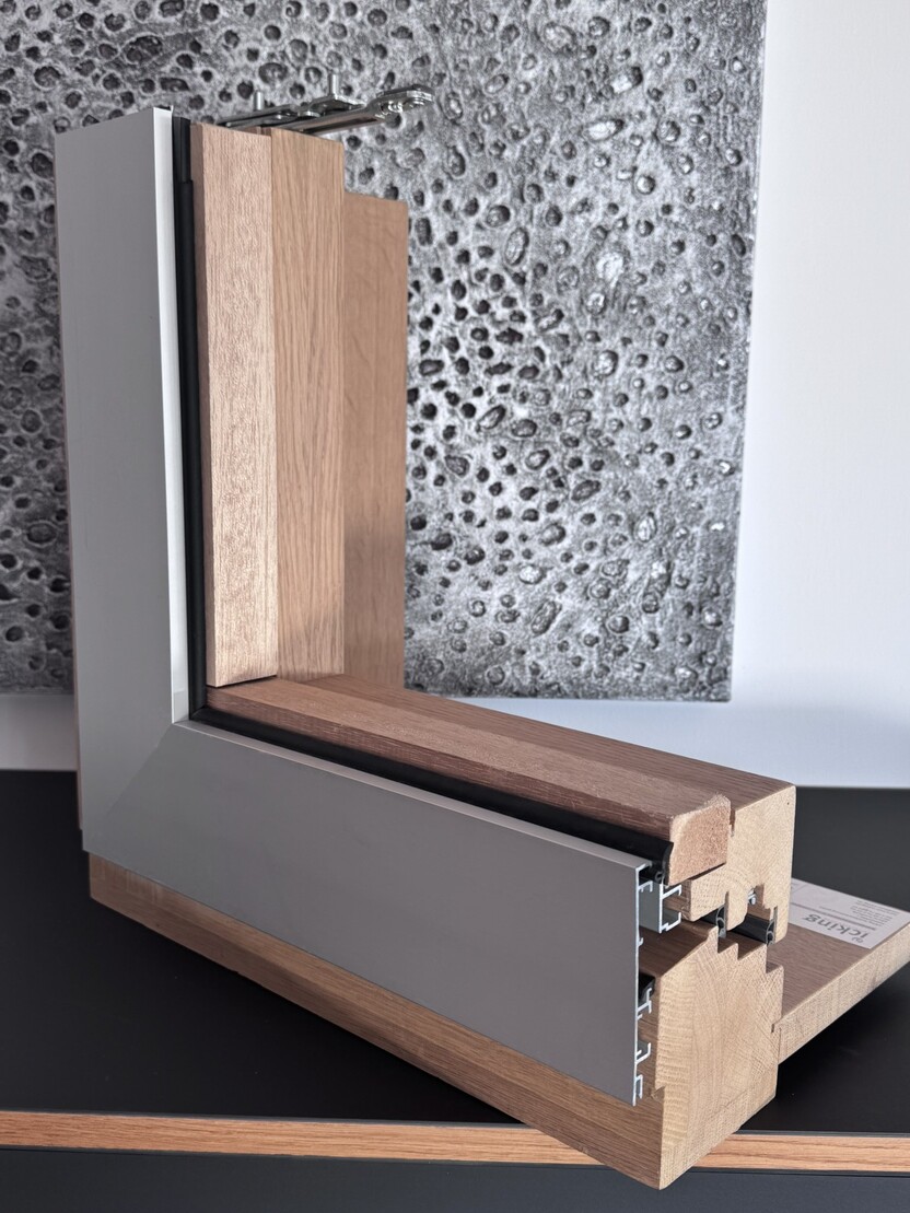 Detailaufnahme eines Fensterrahmens mit Holz- und Metallelementen vor einer strukturierten Wand.