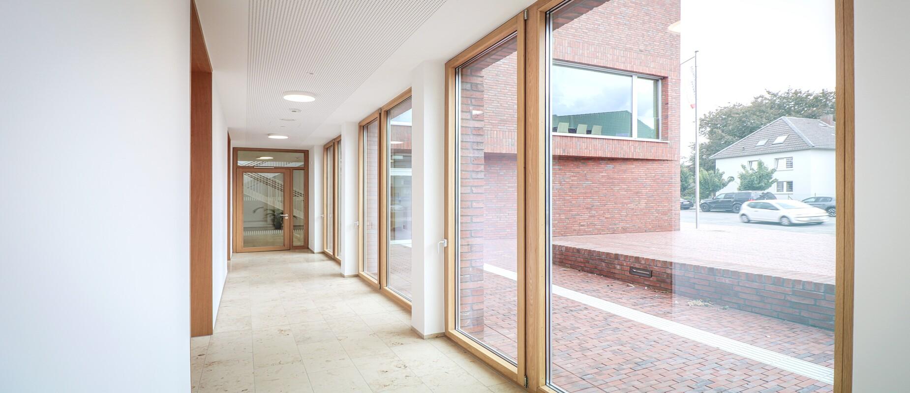 Heller Flur mit gro&szlig;en Fenstern und Sicht auf einen Innenhof, umgeben von roten Backsteinw&auml;nden.