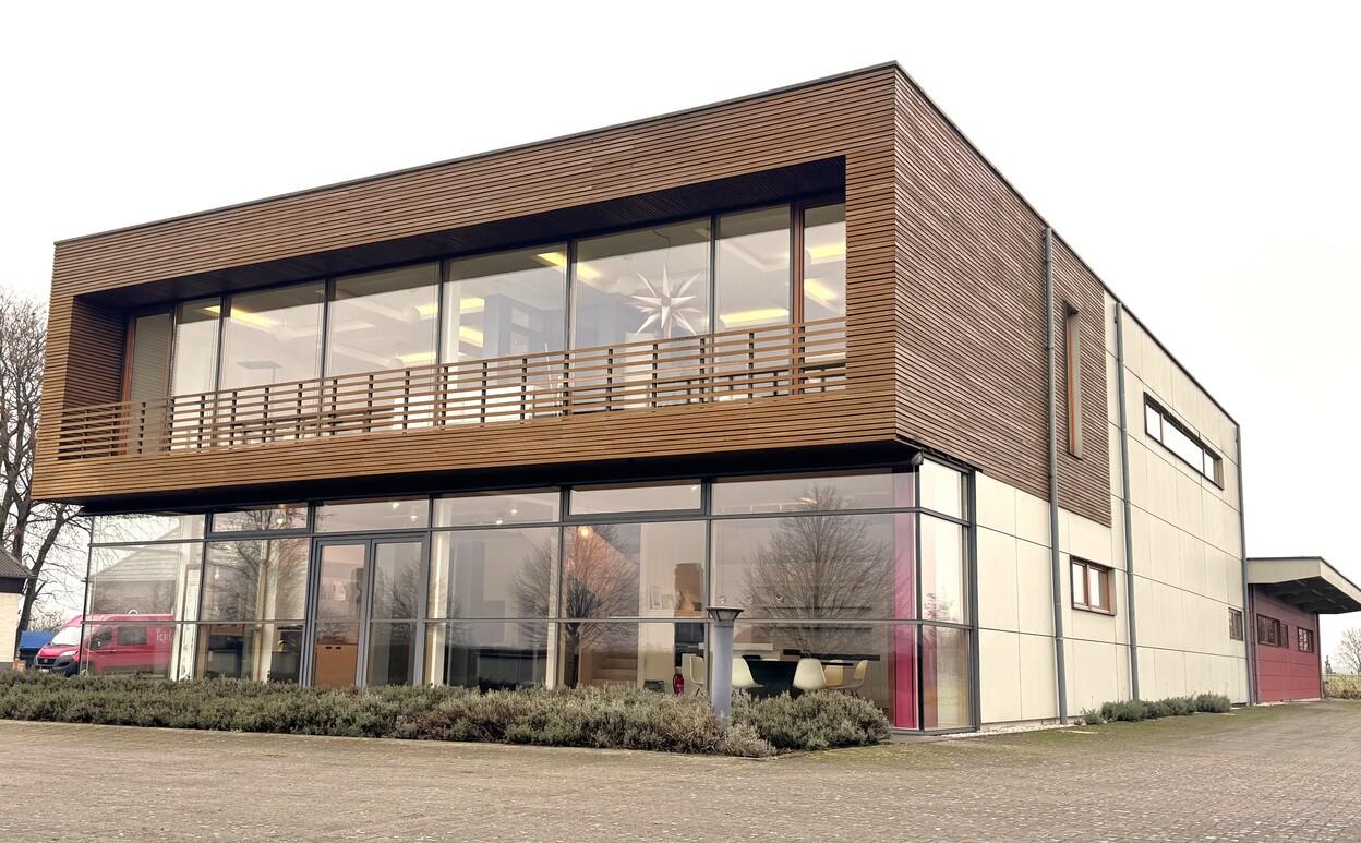 Moderne zweigeschossige Geb&auml;udeansicht mit gro&szlig;en Fenstern und Holzelementen, umgeben von gepflanzten Beeten.