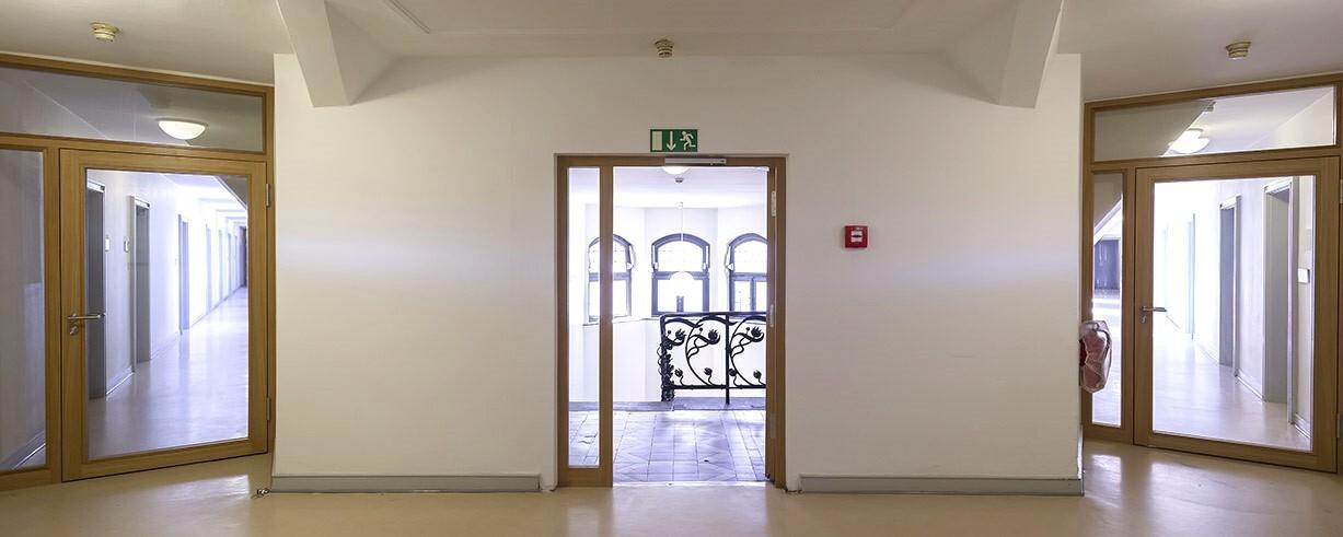 Langer Flur mit Holzrahment&uuml;ren und einer offenen T&uuml;r, die auf einen Balkon mit schmiedeeisernem Gel&auml;nder f&uuml;hrt.