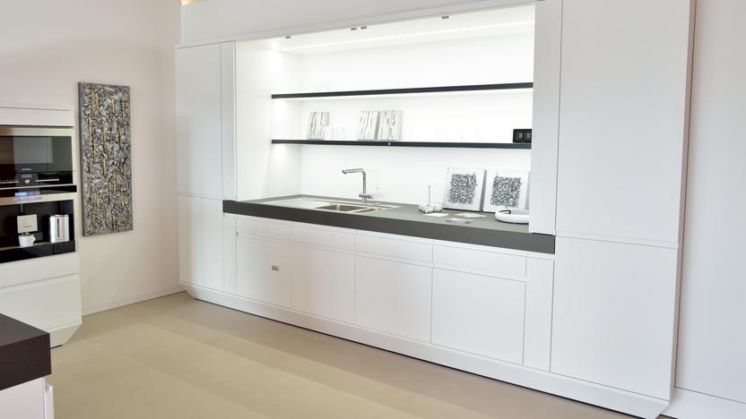 Moderne wei&szlig;e K&uuml;che mit schwarzer Arbeitsfl&auml;che, Sp&uuml;le und offenen Regalen, vor neutralem Hintergrund.