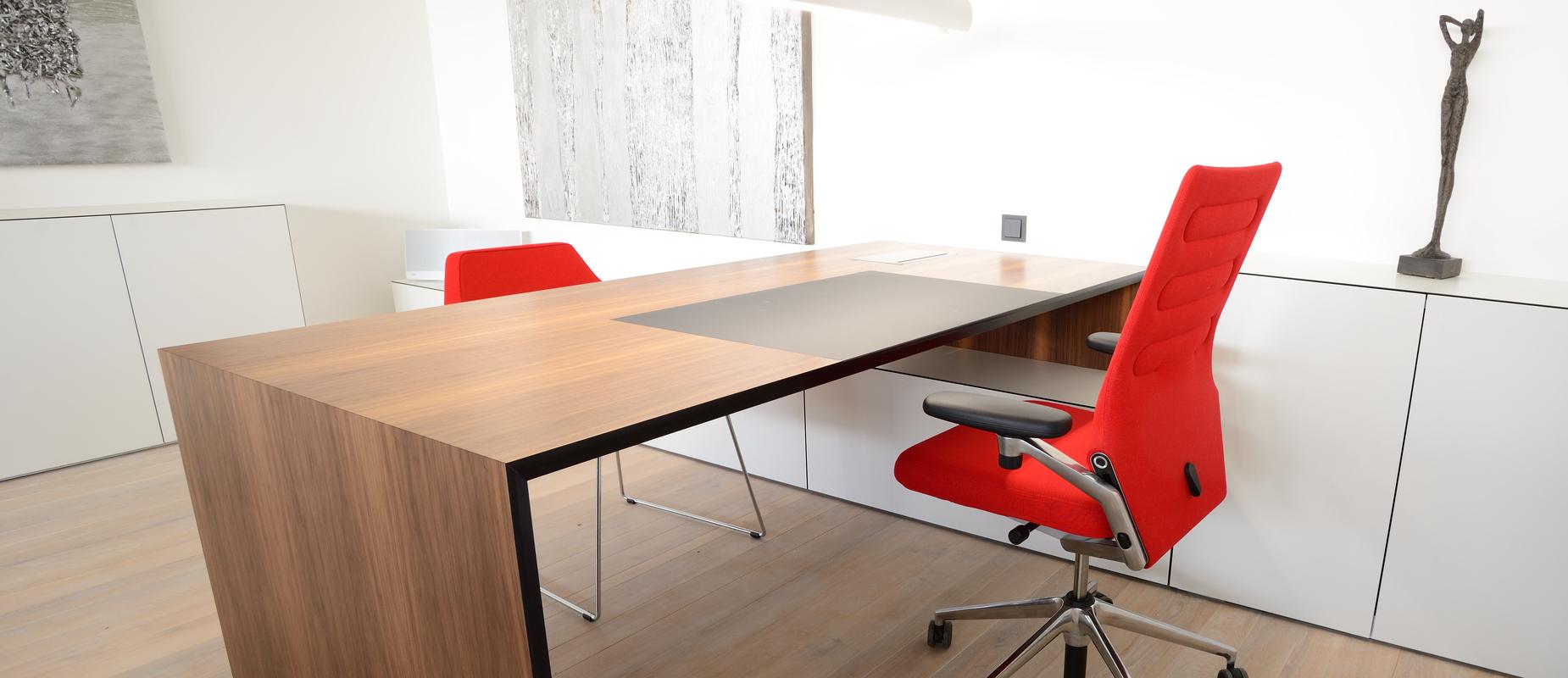 Moderner Arbeitsplatz mit einem Holzschreibtisch, rotem Drehstuhl und minimalistischem Dekor in einem hellen Raum.