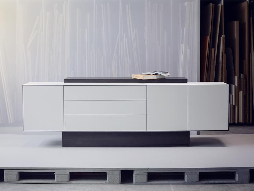 Minimalistisches Sideboard mit Schubladen und offenen F&auml;chern, auf einer Palette in einem modernen Raum.