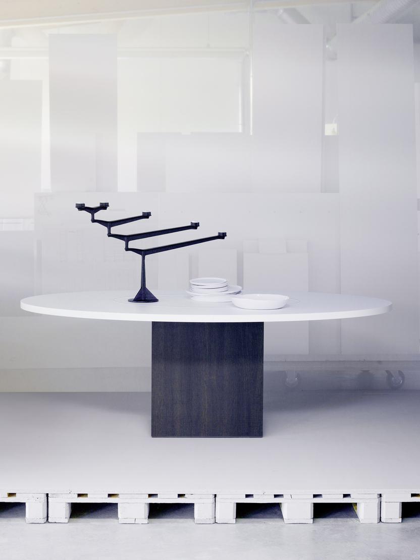 Kreisf&ouml;rmiger Tisch mit schwarzem Gestell und wei&szlig;en Tellern, umgeben von minimalistischer, transparenter Raumgestaltung.