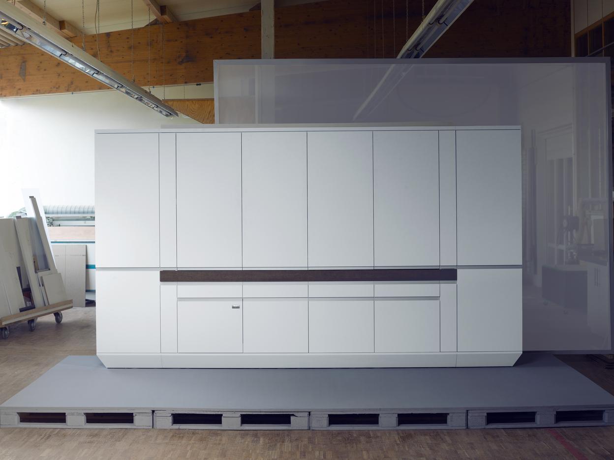 Moderne, wei&szlig;e K&uuml;chenzeile auf einer grauen Plattform in einer hellen Werkstatt. Starke Linien und minimalistische Gestaltung.