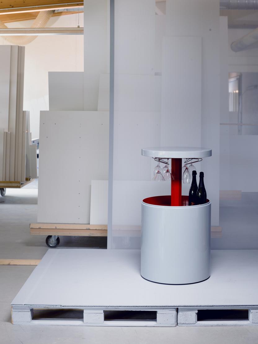 Wei&szlig;er Getr&auml;nkewagen mit roten Akzenten, umgeben von wei&szlig;en Paneelen und einem klaren Raum, im Hintergrund ausgestellte Materialien.
