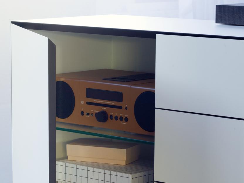 Offene Schublade eines M&ouml;belst&uuml;cks mit einem Radio und mehreren Kisten in neutralen Farben.