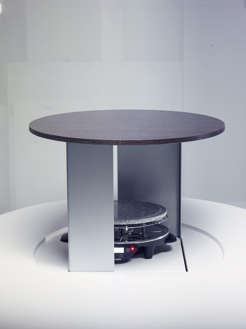 Runde Tischplatte aus Holz &uuml;ber einem grauen Heizger&auml;t in einer modernen, minimalistischen Umgebung.