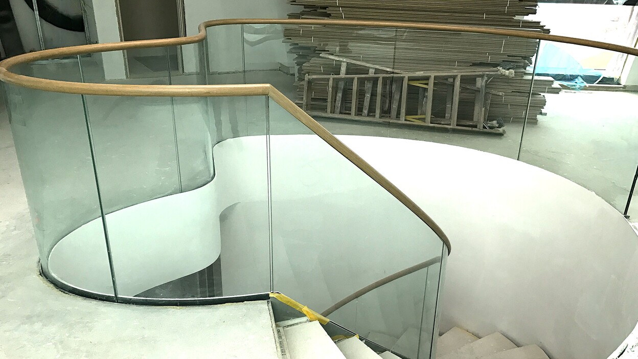 Blick auf eine moderne Wendeltreppe mit Holzhandlauf und Glasgel&auml;nder in einem unfertigen Raum.