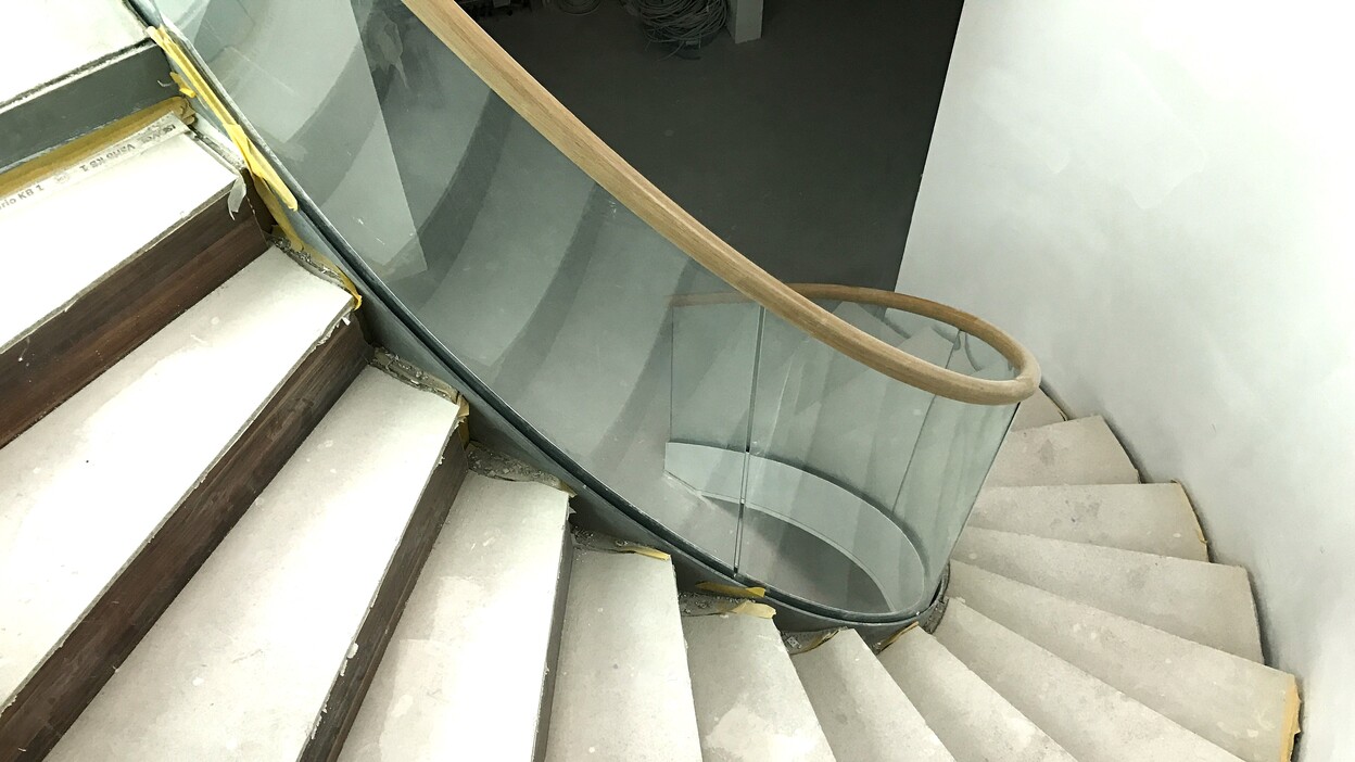 Blick auf eine spiralf&ouml;rmige Treppe mit Holzhandlauf und Glaskapelle in einem unvollendeten Raum.