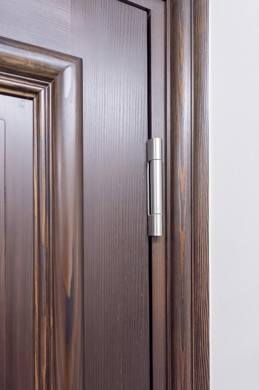 Nahaufnahme eines T&uuml;rscharniers an einer dunklen Holzschiebet&uuml;r mit wei&szlig;em Wandhintergrund.