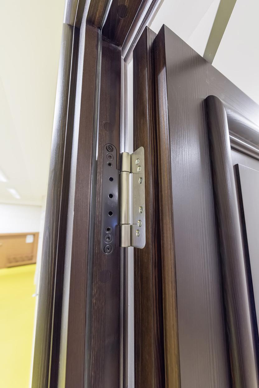 Nahaufnahme eines T&uuml;rscharniers an einer halb ge&ouml;ffneten Holzt&uuml;r in einem hellen Raum.