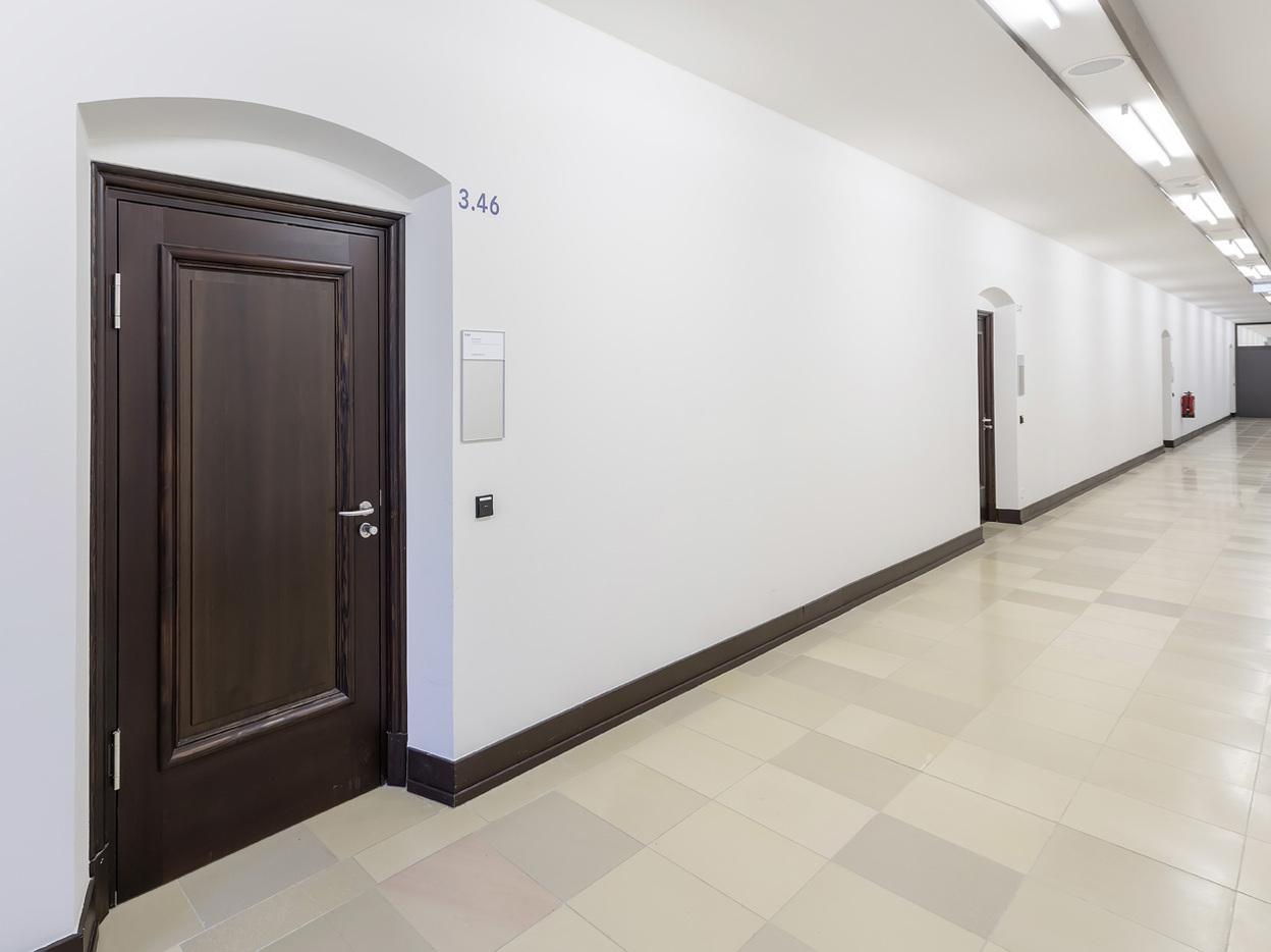 Flur mit mehreren T&uuml;ren und einer Nummerierung an der Wand, helle W&auml;nde und beige Fliesen.