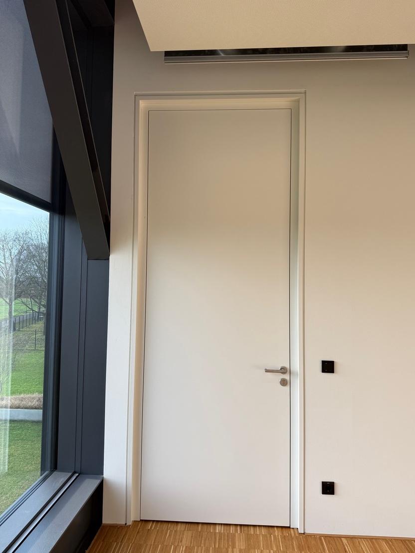 Wei&szlig;e Innent&uuml;r in einem modernen Raum mit Fenster und Wandschalter. Holzfu&szlig;boden ist sichtbar.