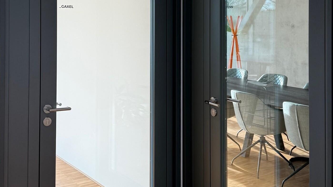 Zwei moderne Glast&uuml;ren mit grauen Rahmungen, die auf einen hellen Raum mit einem Esstisch und St&uuml;hlen blicken.