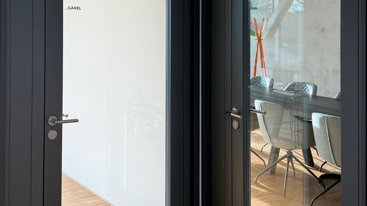 Zwei moderne Glast&uuml;ren mit grauen Rahmungen, die auf einen hellen Raum mit einem Esstisch und St&uuml;hlen blicken.