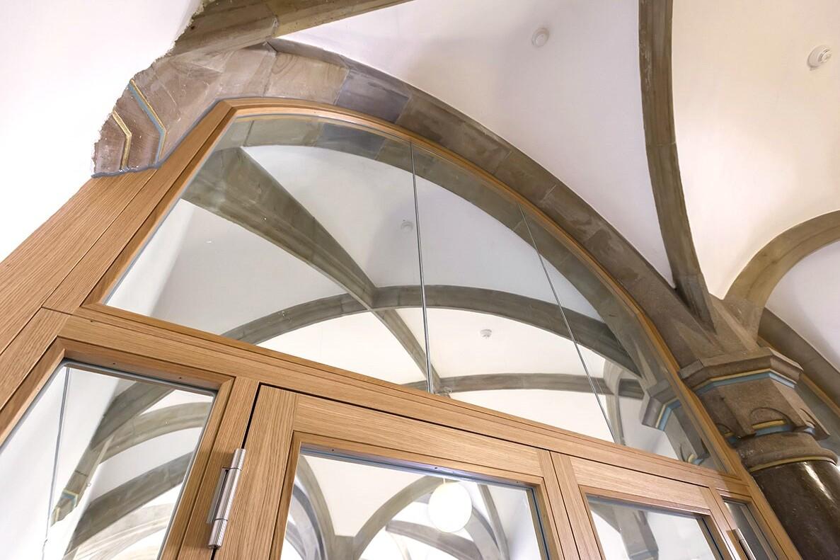 Nahaufnahme einer Holzt&uuml;r mit Glas und detailreichen geschwungenen B&ouml;gen im Hintergrund.