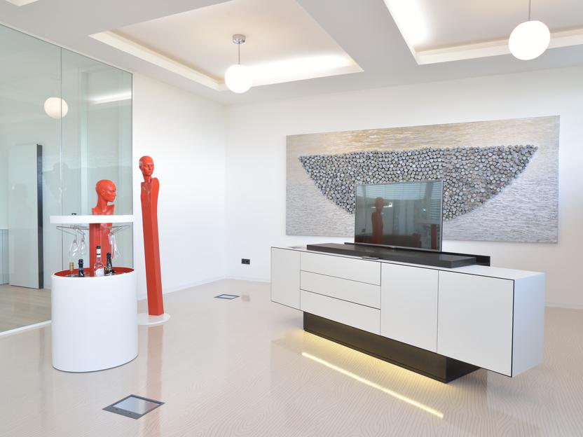 Moderne Wohnraum mit einer wei&szlig;en Anrichte, einem Fernseher und roter Skulptur neben einem Gem&auml;lde auf der Wand.