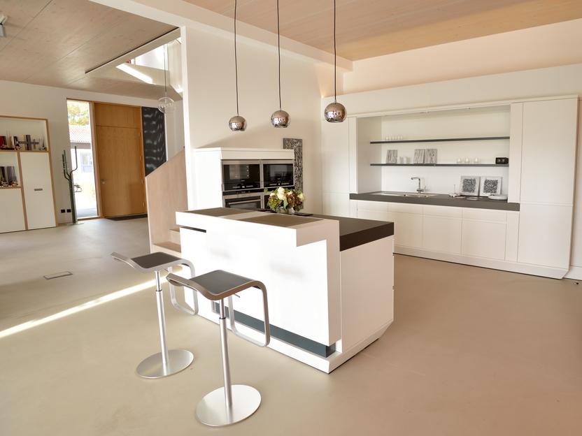 Moderne, helle K&uuml;che mit Kochinsel, integrierten Ger&auml;ten und Barhockern in minimalistischem Design.