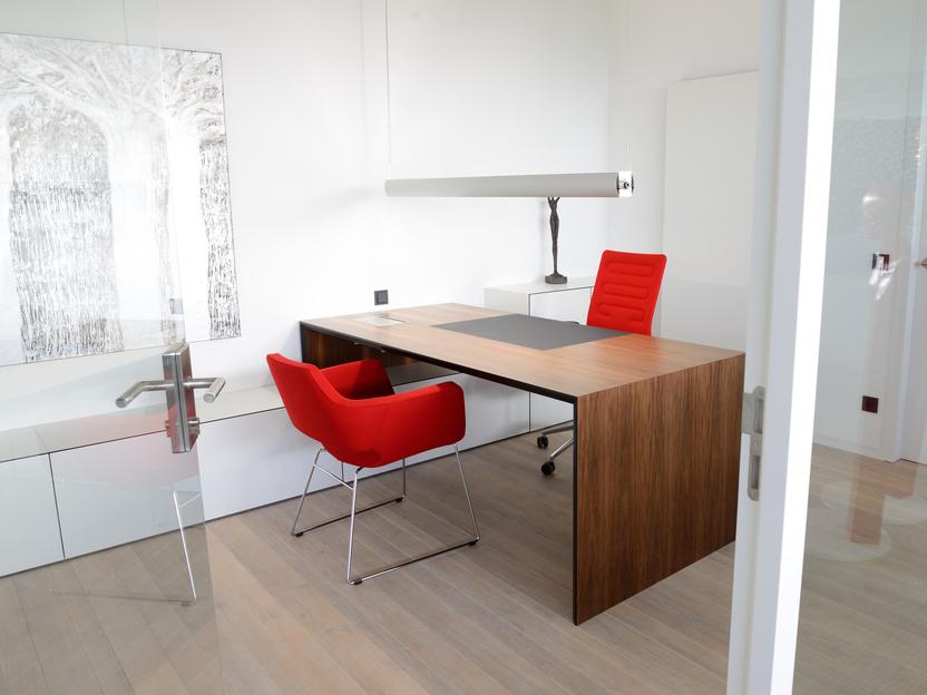 Modernes B&uuml;ro mit Holzschreibtisch, zwei roten St&uuml;hlen und einer gro&szlig;en Lampe, hell und minimalistischen M&ouml;beln.