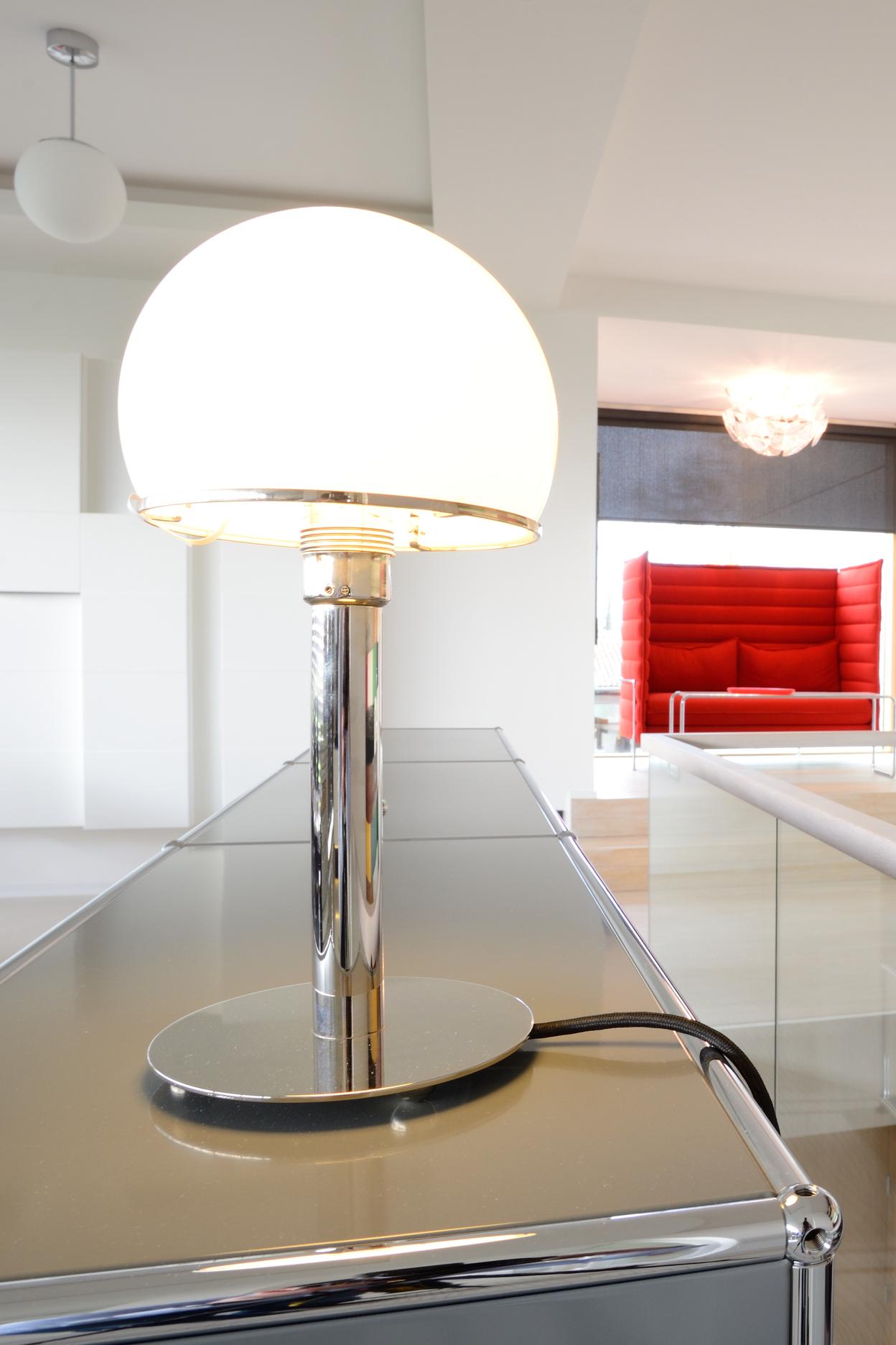 Moderne Innenansicht mit einer Tischlampe, einem Farbwandbild und einem roten Sitzbereich im Hintergrund.