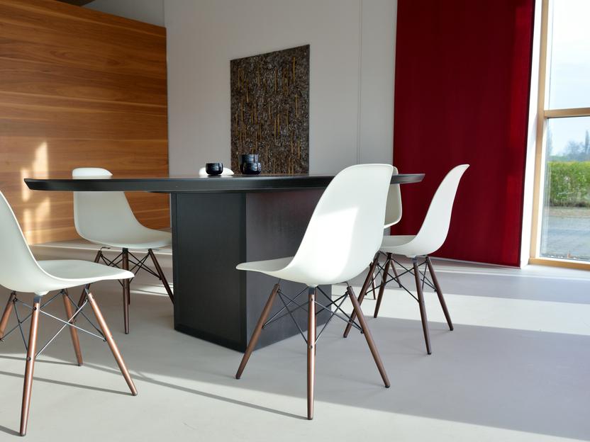 Moderne Essgruppe mit einem schwarzen Tisch und vier wei&szlig;en St&uuml;hlen in einem hellen Raum mit gro&szlig;en Fenstern.