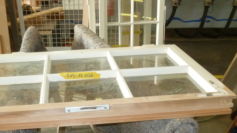 Holzfenster mit mehreren Fenstergl&auml;sern liegt auf einer Werkbank, umgeben von einem gefalteten Tuch.