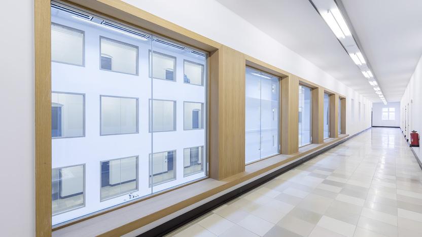 Heller Flur mit gro&szlig;en Fenstern und Holzrahmen, fliesenbedecktem Boden und W&auml;nden in neutralen Farben.