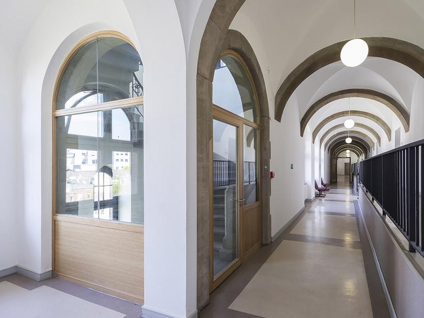 Heller Flur mit hohen B&ouml;gen, Fenster und T&uuml;ren, M&ouml;bel auf der linken Seite, in modernes Architekturdesign integriert.