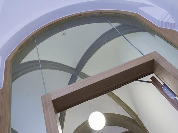 Blick auf eine moderne Glast&uuml;r mit Holzrahmen unter einer gew&ouml;lbten Decke und einer h&auml;ngenden Lampe.