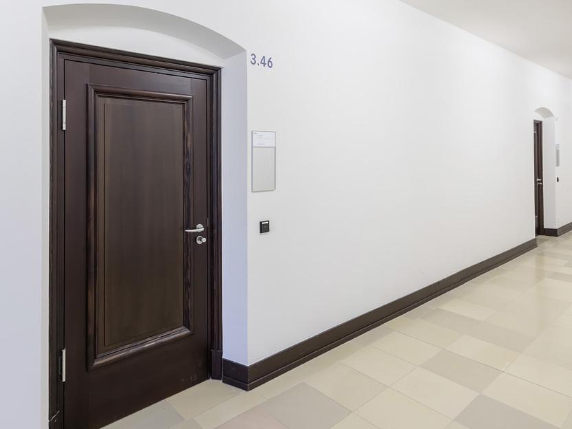 Flur mit drei T&uuml;ren und neutralen W&auml;nden, hell erleuchtet durch Deckenleuchten. T&uuml;r 3.46 links im Bild.