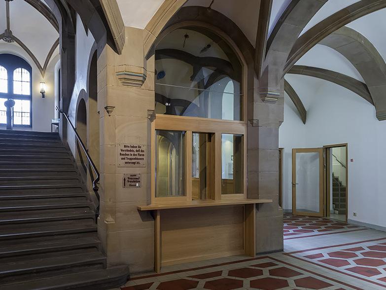 Foyer mit Treppe, Empfangstresen und gro&szlig;en Fenstern, beeindruckende Architektur mit hohen Decken.
