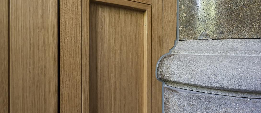 Detailaufnahme einer Holzverkleidung neben einem grauen S&auml;ulenschaft aus Stein.