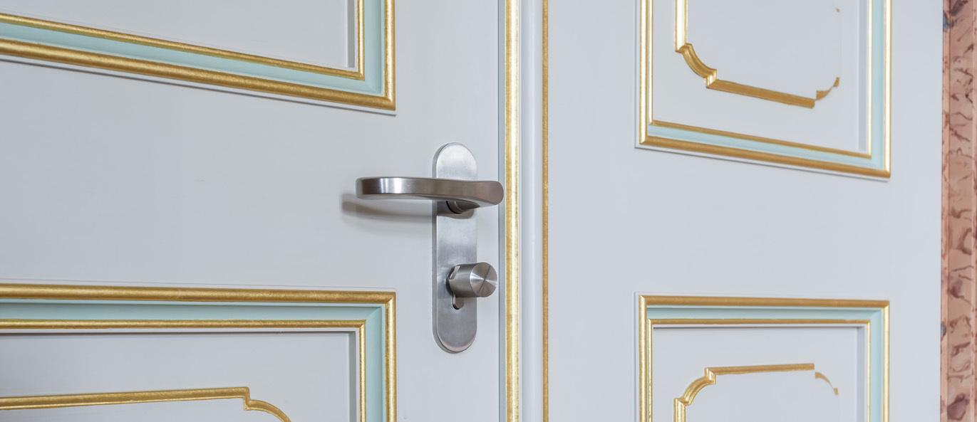 Nahaufnahme einer wei&szlig;en T&uuml;r mit goldenen Verzierungen und einer modernen T&uuml;rklinke.