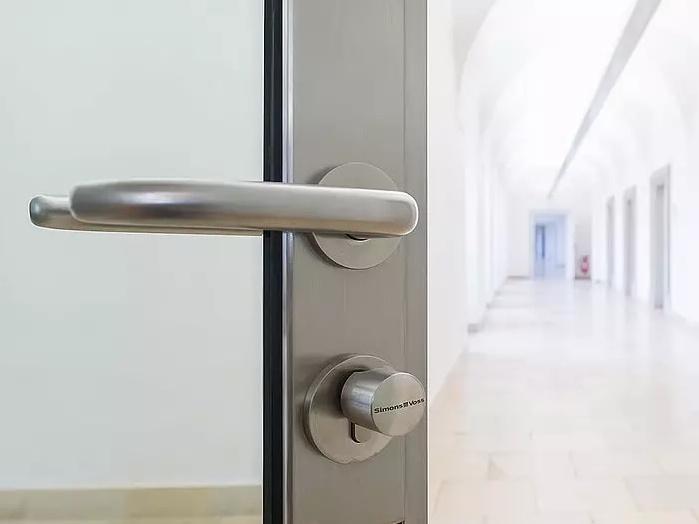 T&uuml;ransicht mit modernem Beschlag, Blick auf einen hellen Flur mit langen W&auml;nden und B&ouml;gen.